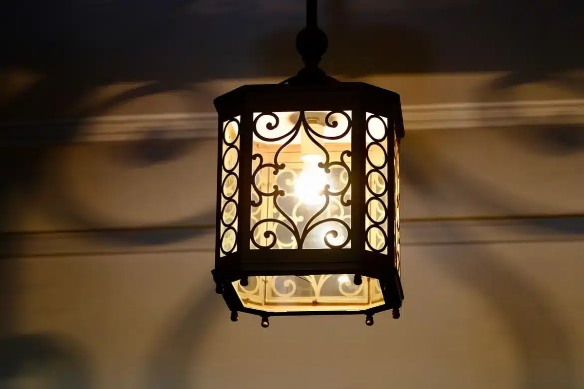 Vieille passoire métallique transformée en luminaire suspendu à une pergola, éclairée de l'intérieur