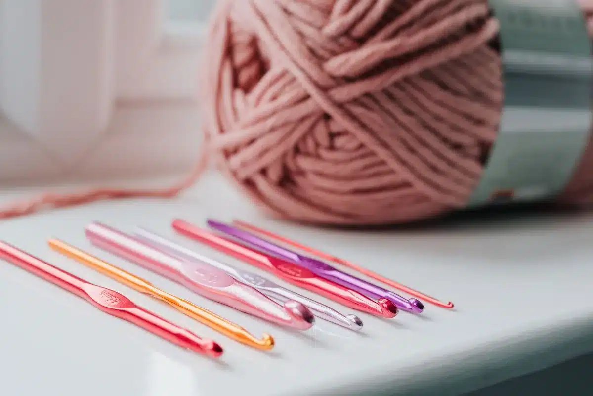 Différentes épaisseurs de laine avec aiguilles de tricot de tailles variées sur une surface neutre.