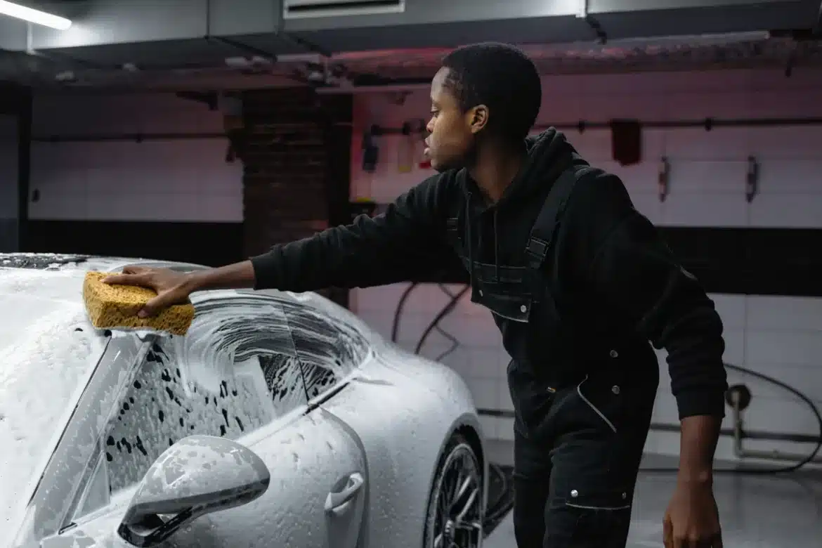 Mains gantées de microfibre lavant une carrosserie brillante avec un jet d'eau doux