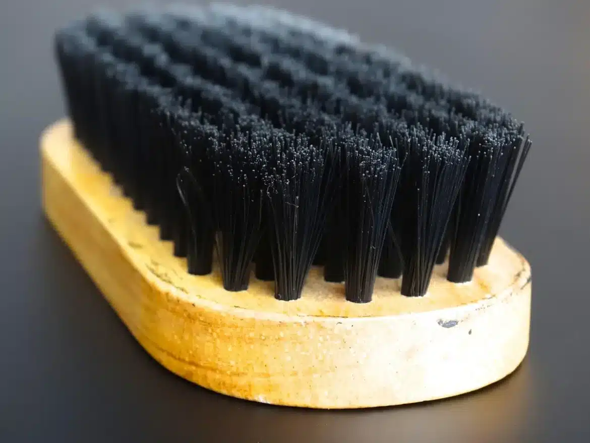 Mains nettoyant une sneaker blanche avec une brosse douce au-dessus d'eau savonneuse